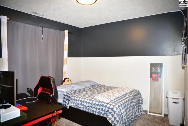 Modern bedroom with a gaming setup, a queen bed with a geometric comforter, and two-tone walls.