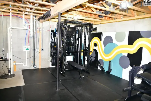 Home gym with black rubber flooring, a multi-station weight machine, and a colorful abstract mural.
