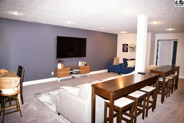 Spacious finished basement with a gray accent wall, mounted TV, and a long wooden bar with stools.