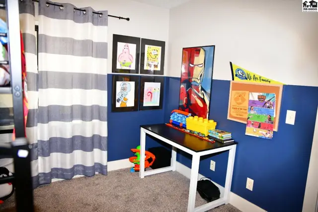 Children's room with blue and white walls, a desk, and superhero and cartoon artwork.