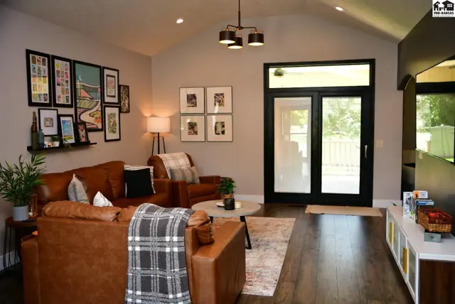 Spacious living room with vaulted ceiling, leather sectional, and large glass doors leading outdoors.