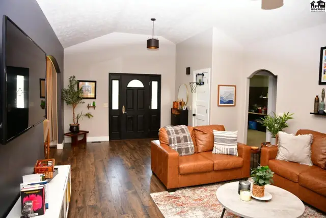 Spacious living room with vaulted ceilings, leather sofas, and dark wood floors leading to a grand black double door entrance.