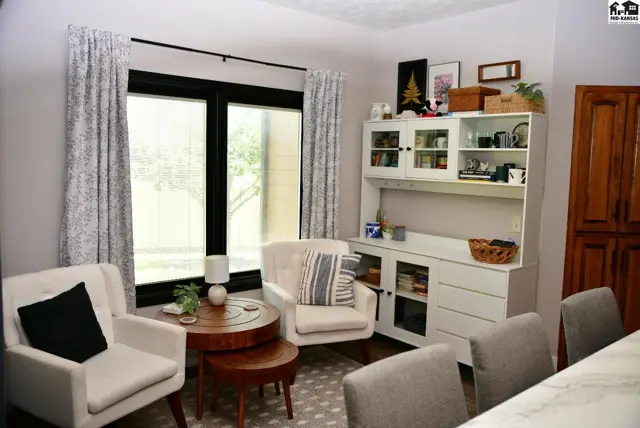 Cozy living area with two armchairs, a round coffee table, and a white hutch against a large window.