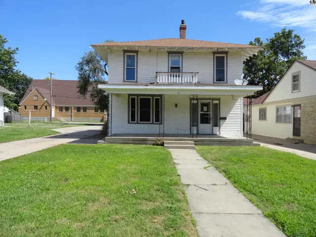 White two-story house with a covered porch, balcony, and a concrete walkway leading to the front door.