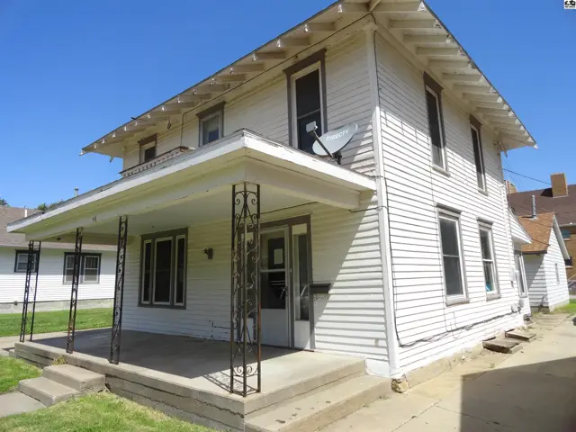 Exterior of a two-story white vinyl-sided house with a covered porch and decorative metal posts.