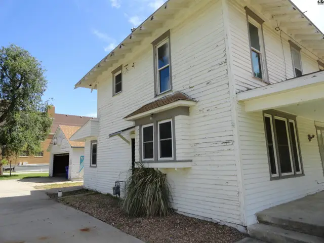 Exterior of a white clapboard house with gray trim, featuring a covered porch and detached garage.