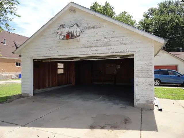 Two-car garage with weathered white siding, a basketball hoop, and a concrete driveway.