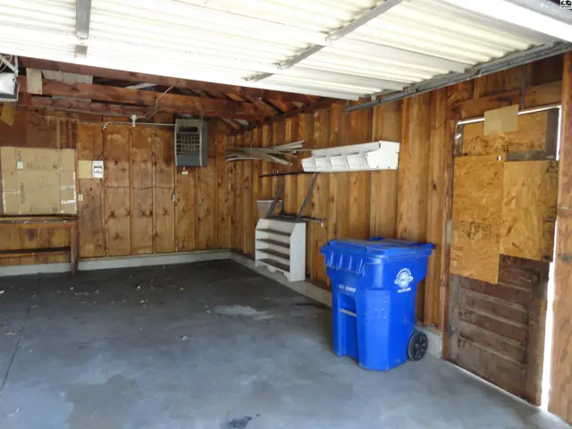 A spacious garage with wood-paneled walls, concrete floor, and a blue trash bin.