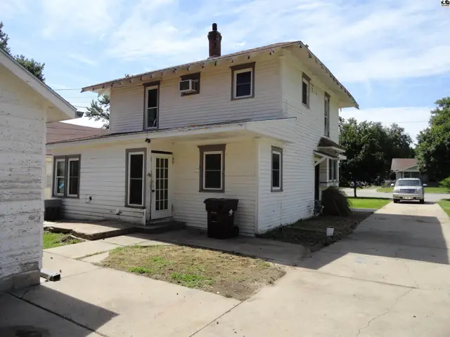 Two-story white clapboard house with gray trim, a chimney, and a concrete driveway.