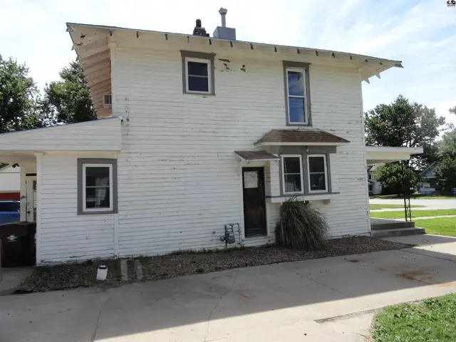 Exterior of a white, two-story house with weathered siding, a bay window, and a covered porch.
