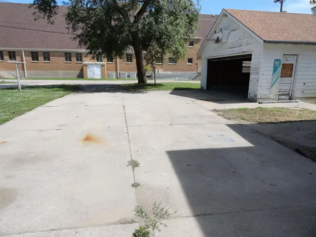 Concrete driveway leads to a detached garage with a white exterior and wooden doors.