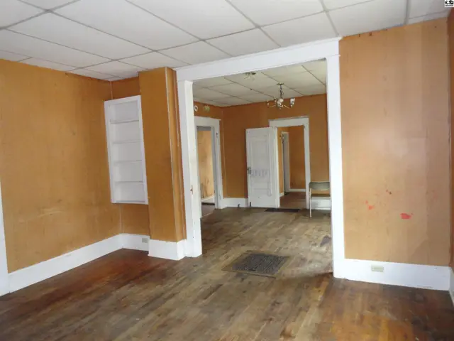 Interior view of a room with orange walls, white trim, hardwood floors, and an open doorway to another room.