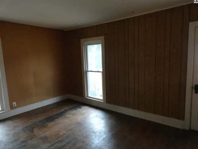 Empty room with wood-paneled walls, a single window, and distressed hardwood floors.