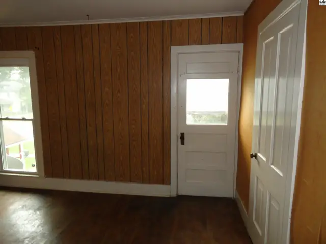 Interior room with wood-paneled walls, a white door with a glass pane, and a window.