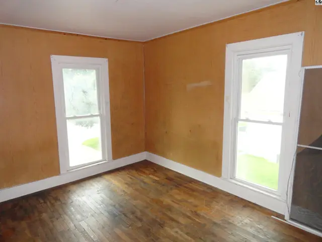 Corner of a room with orange walls, white trim, and distressed hardwood floors.