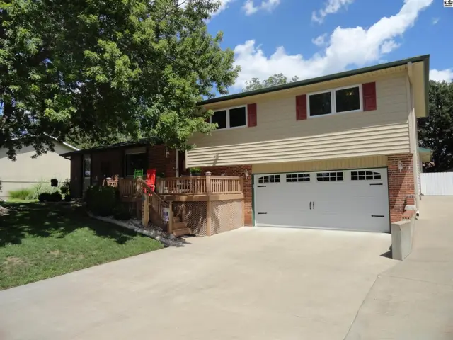 Two-story home with tan siding, brick accents, red shutters, and a large white garage door.