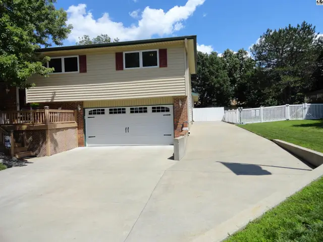 Two-story home with beige siding, red shutters, and a white garage door on a concrete driveway.