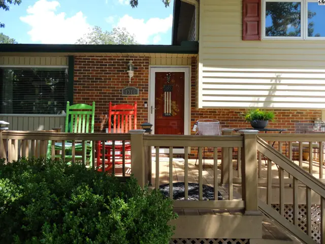 Front porch with colorful rocking chairs, brick and siding exterior, and wooden railings.