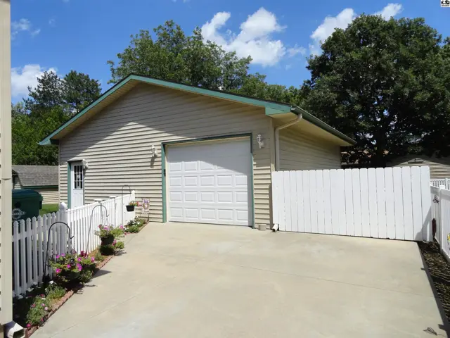 Exterior view of a beige vinyl-sided home with a white garage door and white picket fence.