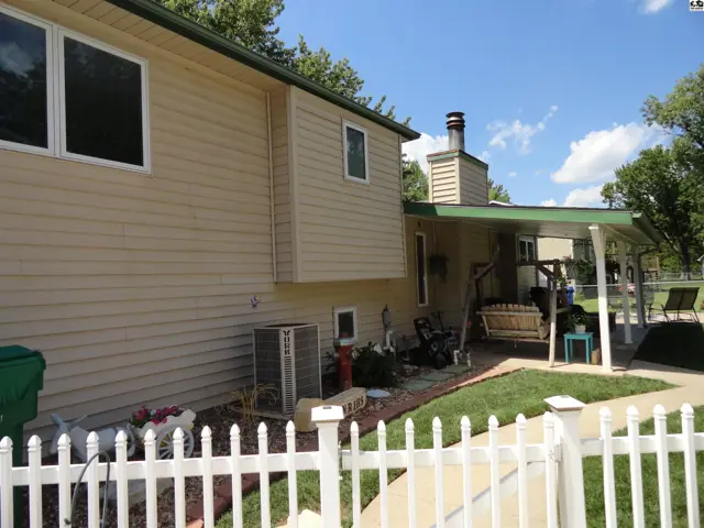 Tan siding home with a covered patio, white picket fence, and outdoor seating.