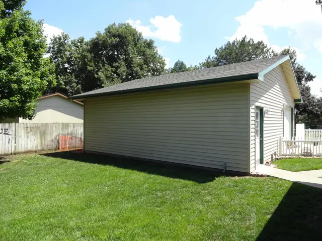Exterior view of a tan vinyl-sided garage with a green trim and a paved walkway.