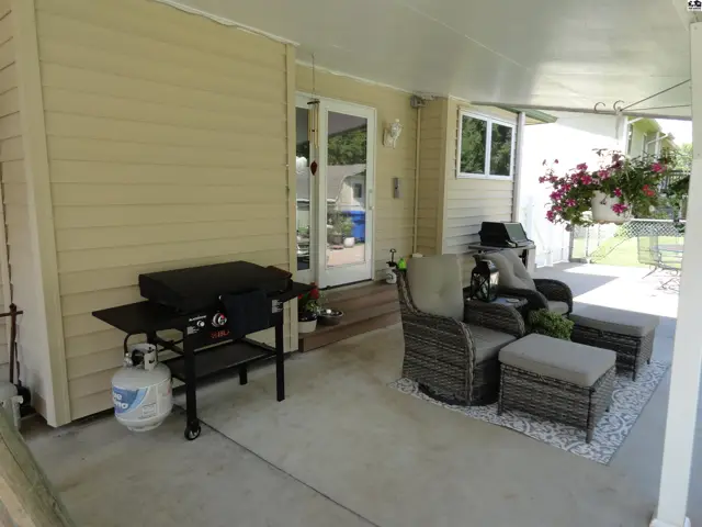 Covered patio with seating, grill, and hanging flowers offers outdoor living space.