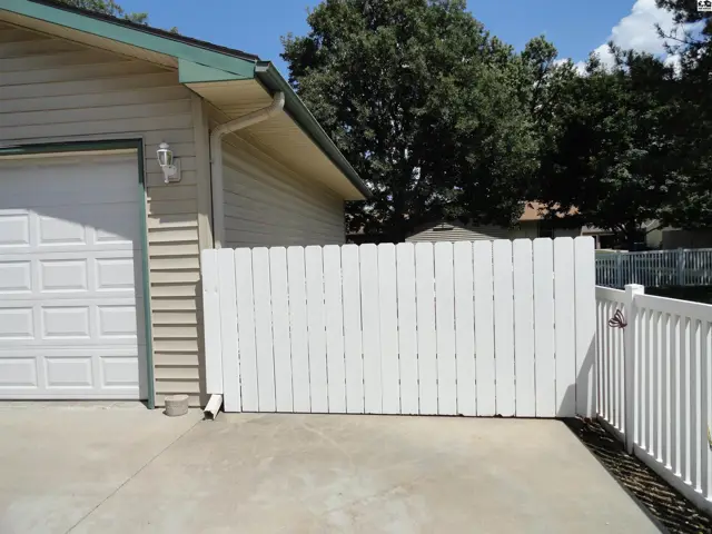 White picket fence and garage door on a concrete driveway with siding and green trim.