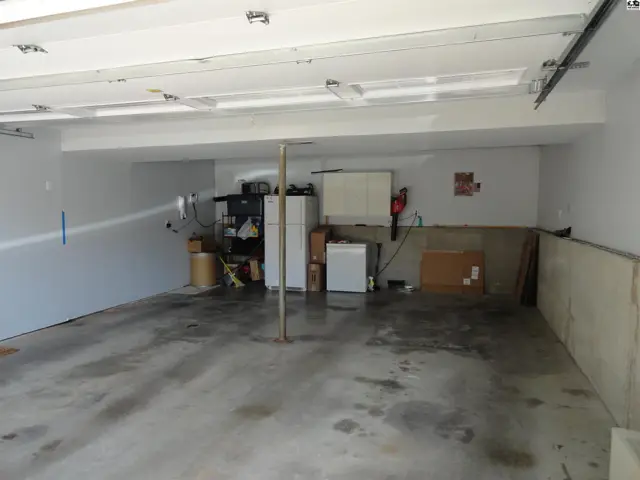 Spacious garage with concrete floor, white walls, and overhead lighting, featuring appliances and storage.