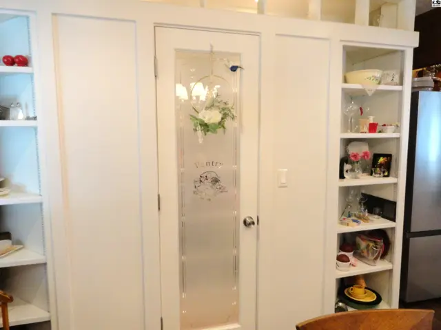 Frosted glass pantry door with decorative wreath, flanked by white built-in shelves displaying various items.