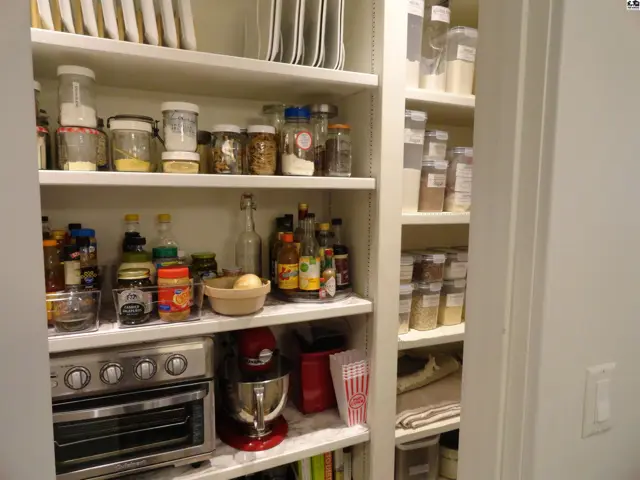A well-organized pantry with white shelves stocked with food, appliances, and kitchenware.