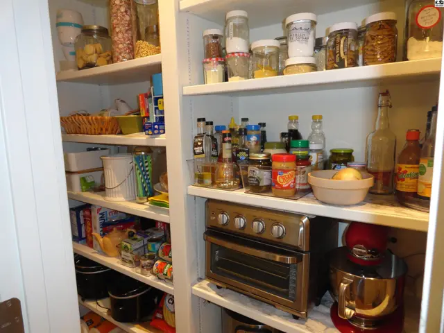 Well-stocked pantry with white shelves showcasing jars, boxes, a toaster oven, and a red stand mixer.