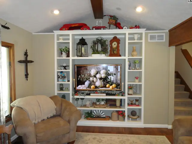 Built-in white shelving unit with a television and decorative items, flanking a plush armchair.
