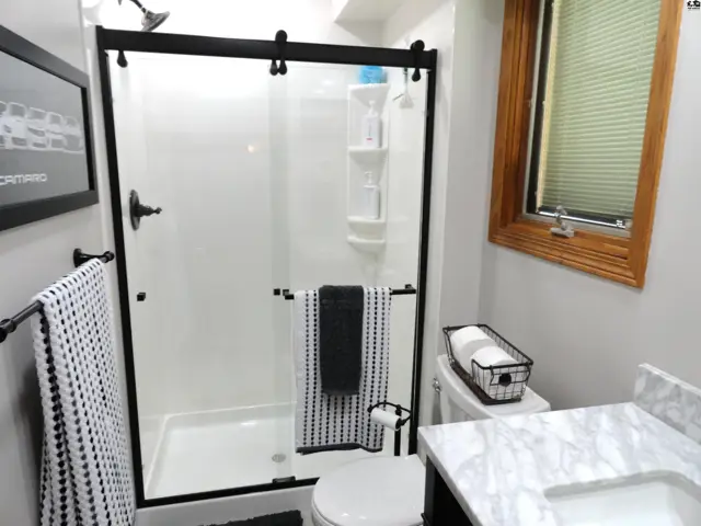 Modern bathroom with a sleek white shower stall, marble vanity, and black accents.