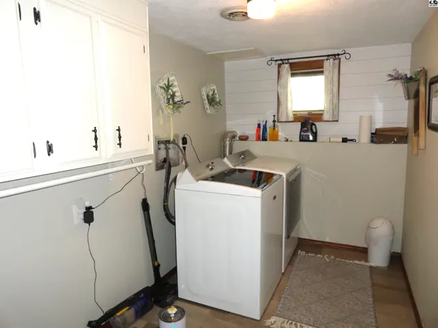 Laundry room with white cabinets, washer, dryer, shiplap accent wall, and wood-look flooring.