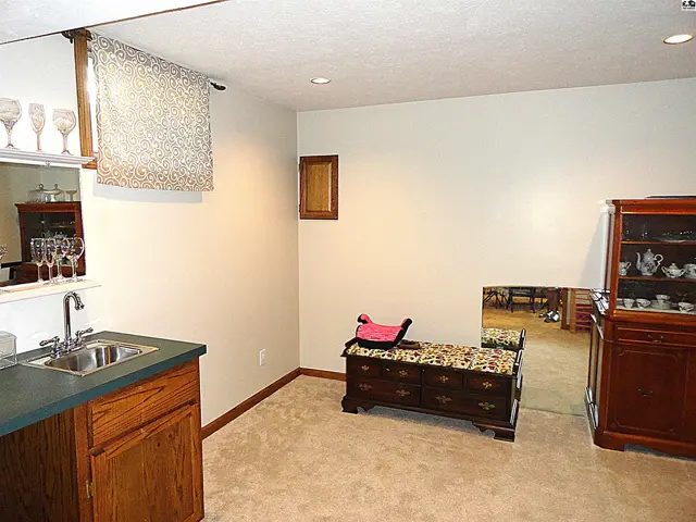 Finished basement with wet bar, carpet, wood cabinetry, and antique chest.