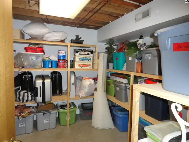 A cluttered basement storage room with wooden shelves filled with boxes, luggage, and household items.
