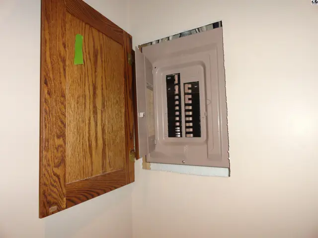 Open wooden cabinet reveals a residential electrical breaker panel with visible breakers.