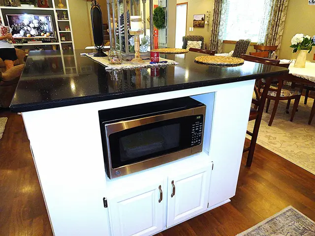 Kitchen island with black granite countertop, stainless steel microwave, and white cabinetry.