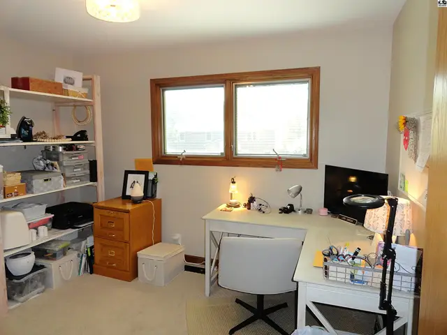 Bright home office with a corner desk, filing cabinet, and shelves filled with supplies.