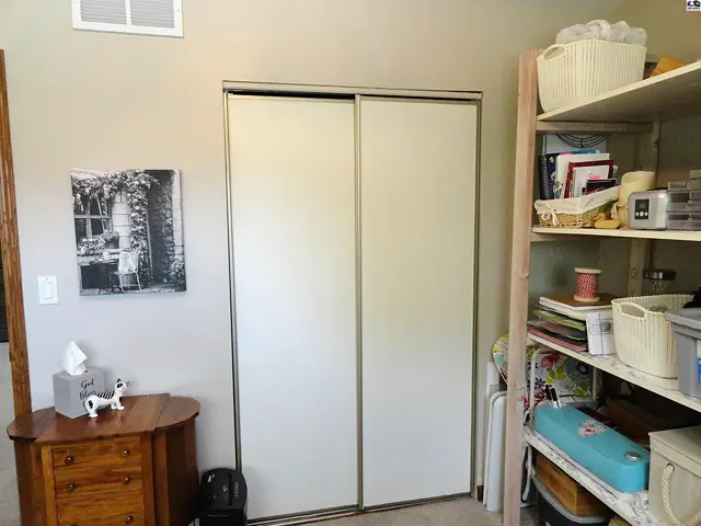 Closet with sliding white doors, next to a wooden dresser and a tall shelf unit.