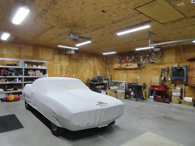 Spacious garage with a car cover, bicycles, shelving, and workshop equipment.