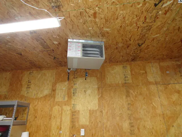 Garage ceiling heater mounted on exposed wood paneling walls with fluorescent lighting.