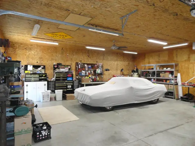 Spacious garage with a covered car, tool chests, shelving, and wood-paneled walls.