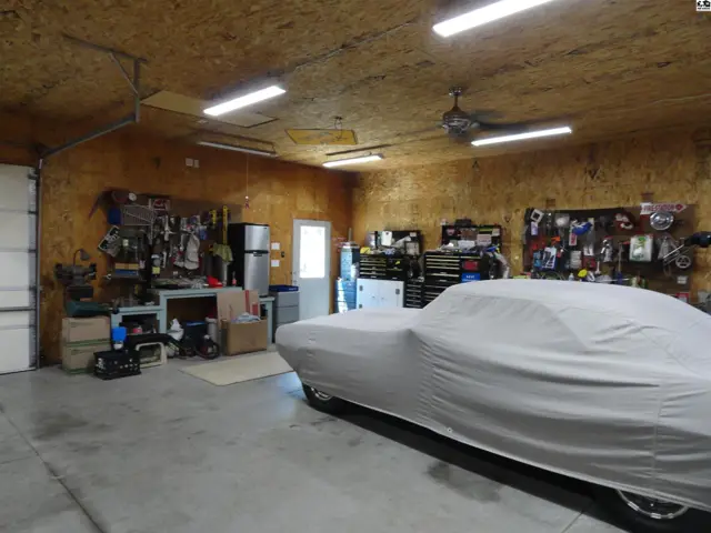 Spacious garage with concrete floor, wood-paneled walls, and a car covered with a light gray tarp.