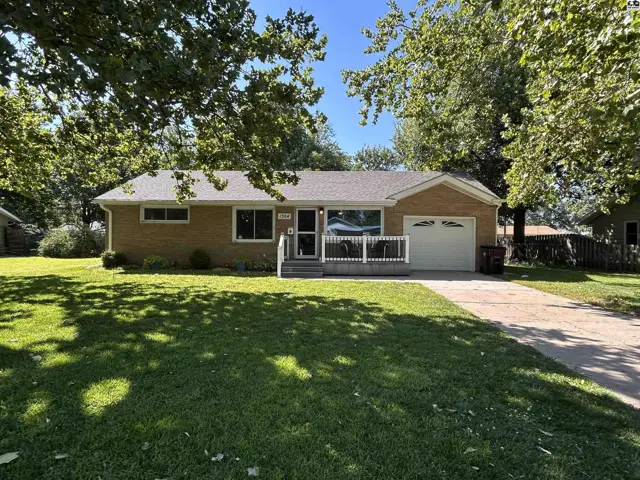 Brick ranch home with a covered porch, attached garage, and mature trees in a grassy yard.