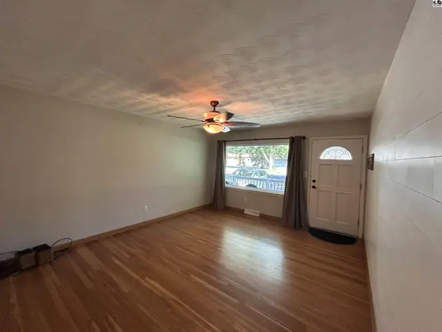 Spacious living room with hardwood floors, large window, and a white front door.