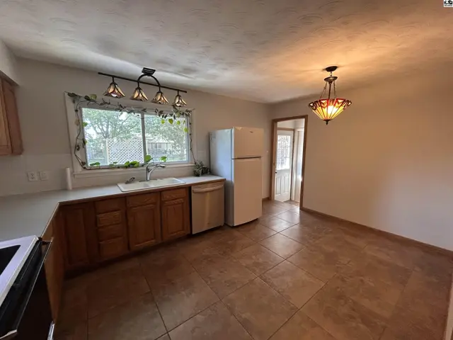 Kitchen with wood cabinets, white countertops, tiled floor, and a large window.