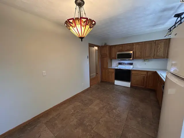 Kitchen with wood cabinets, white appliances, and tiled flooring under a decorative pendant light.