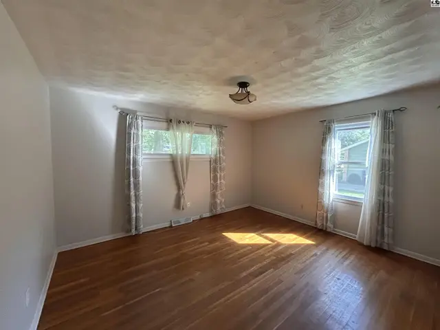 Bright bedroom with hardwood floors, textured ceiling, and two windows with patterned curtains.