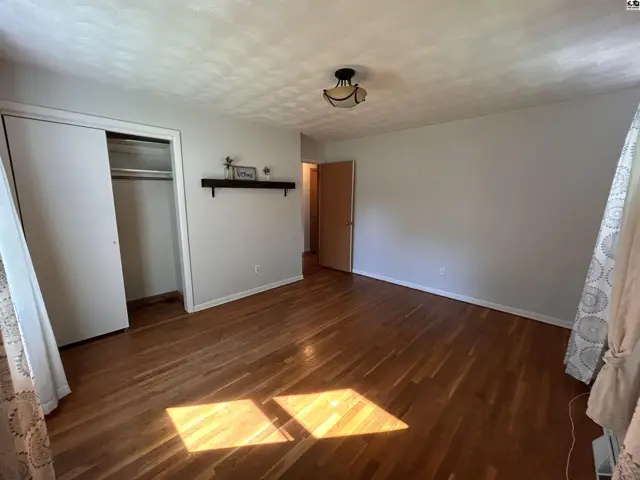 Spacious bedroom with hardwood floors, white closet doors, and a decorative ceiling light fixture.